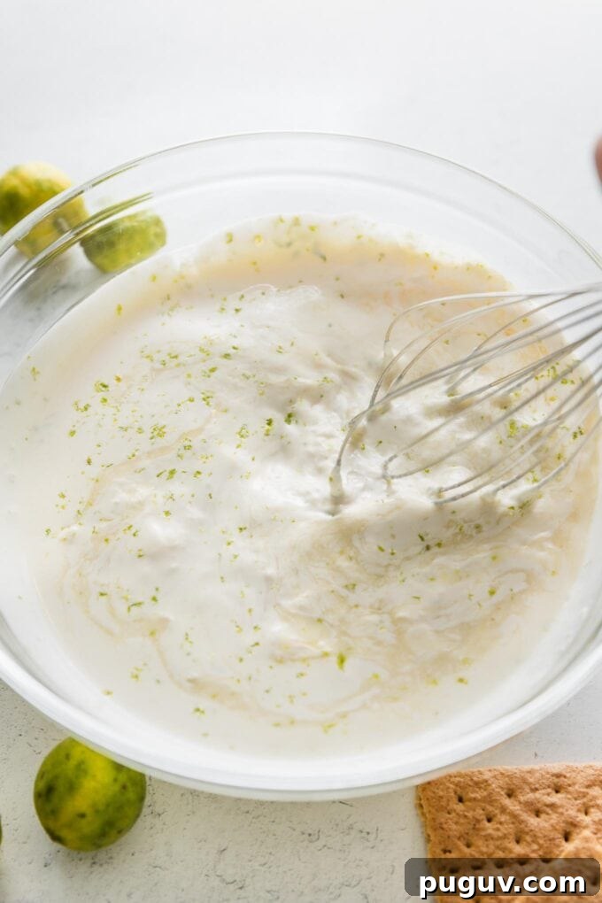 Action shot of a large metal whisk incorporating lime juice and zest into a cream mixture.