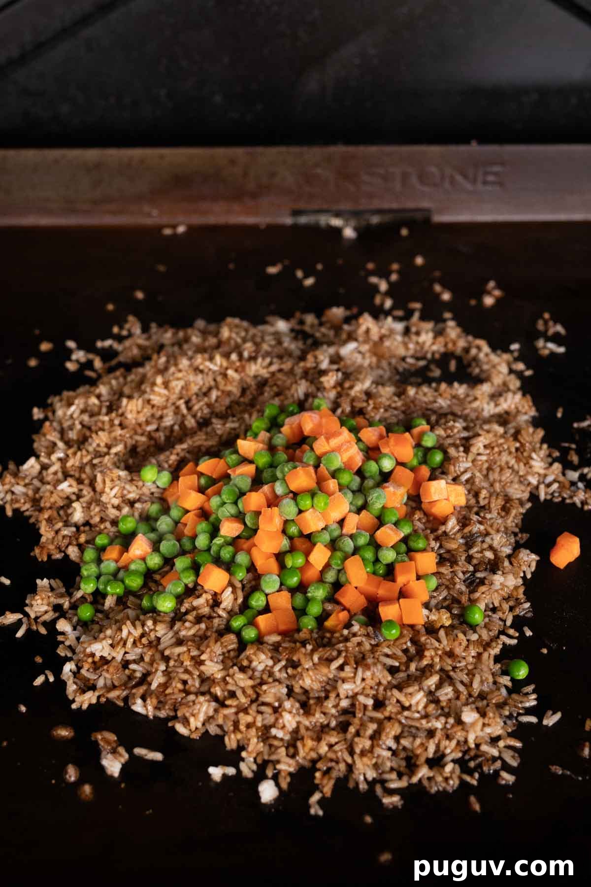 Cooked seasoned rice topped with diced carrots and peas on the griddle