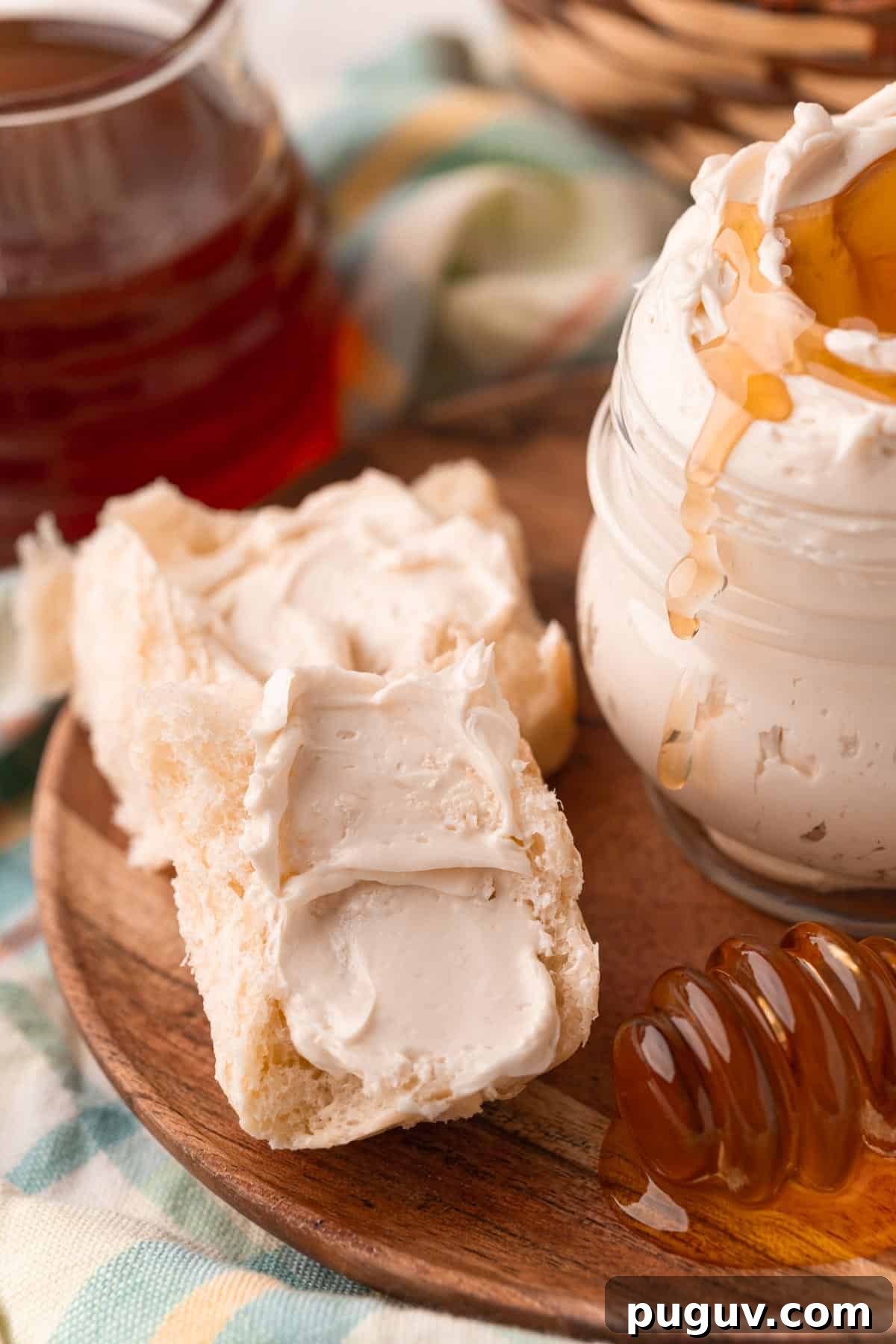 Light and Fluffy Honey Whipped Butter for Toast and Baking 4 Dinner rolls halves slathered with whipped honey butter next to a jar of it on a wooden plate.