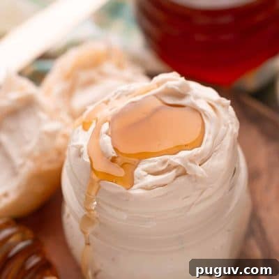 Light and Fluffy Honey Whipped Butter for Toast and Baking 6 Honey butter in a glass jar on a wooden plate with a roll next to it.