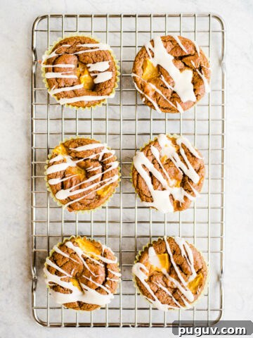 Peach muffins with icing on a rack.