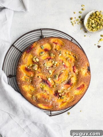 A cake with peaches and pistachios on a wire rack.