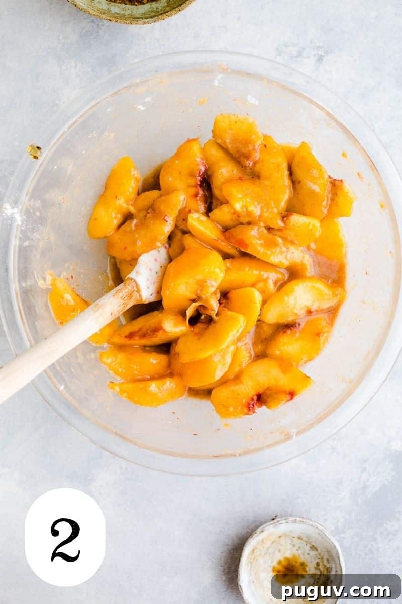 Gluten-Free Peach Oat Crumble Recipe for Summer Desserts 5 Peaches mixed with arrowroot and spices into a syrupy mixture in a glass mixing bowl.