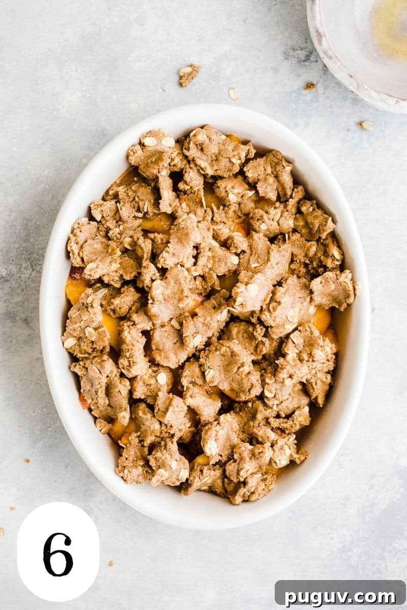 Gluten-Free Peach Oat Crumble Recipe for Summer Desserts 9 Peaches topped with oat flour and oat crumble dough in a white baking dish.