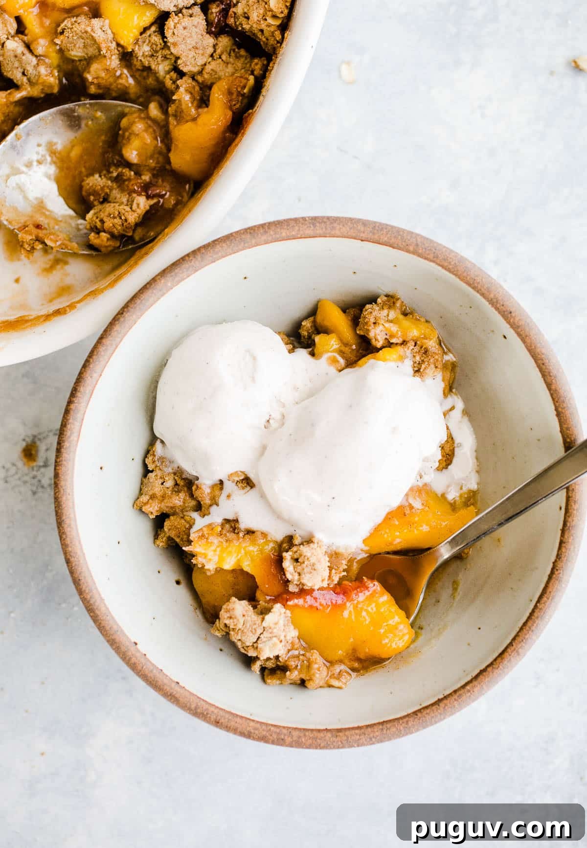 Gluten-Free Peach Oat Crumble Recipe for Summer Desserts 10 Baked peach crumble serving in a bowl topped with vanilla ice cream.