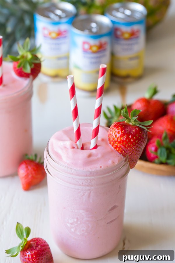 Pineapple Strawberry Cream Slush Recipe — Refreshing Tropical Drink 2 Dole Pineapple Strawberry Cream Slush in a glass jar, with two straws and a strawberry on the rim of the jar.