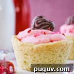 Close up shot of a cookie cup on a white plate with chocolate hearts scattered around with a pink background.