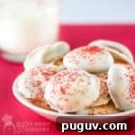 Side view of a white plate with multiple Valentines Day cookies with a clear glass of milk in the background.