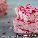 Side view of three stacked strawberry fudge pieces sprinkled with red and pink sprinkles.