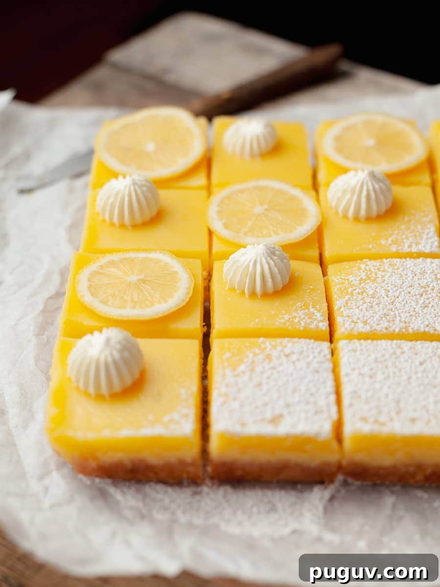 Gluten-Free Lemon Bars Recipe with Tangy Shortbread Crust 2 gluten free lemon bars with a shortbread crust topped with powdered sugar, whipped cream and slices of lemons on parchment paper