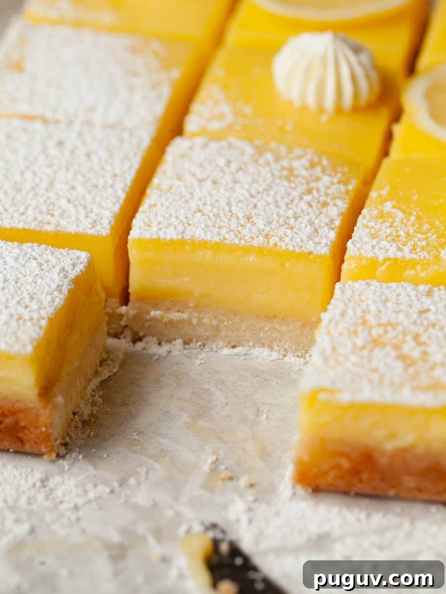 Gluten-Free Lemon Bars Recipe with Tangy Shortbread Crust 9 lemon bars with a shortbread crust topped with powdered sugar on parchment paper