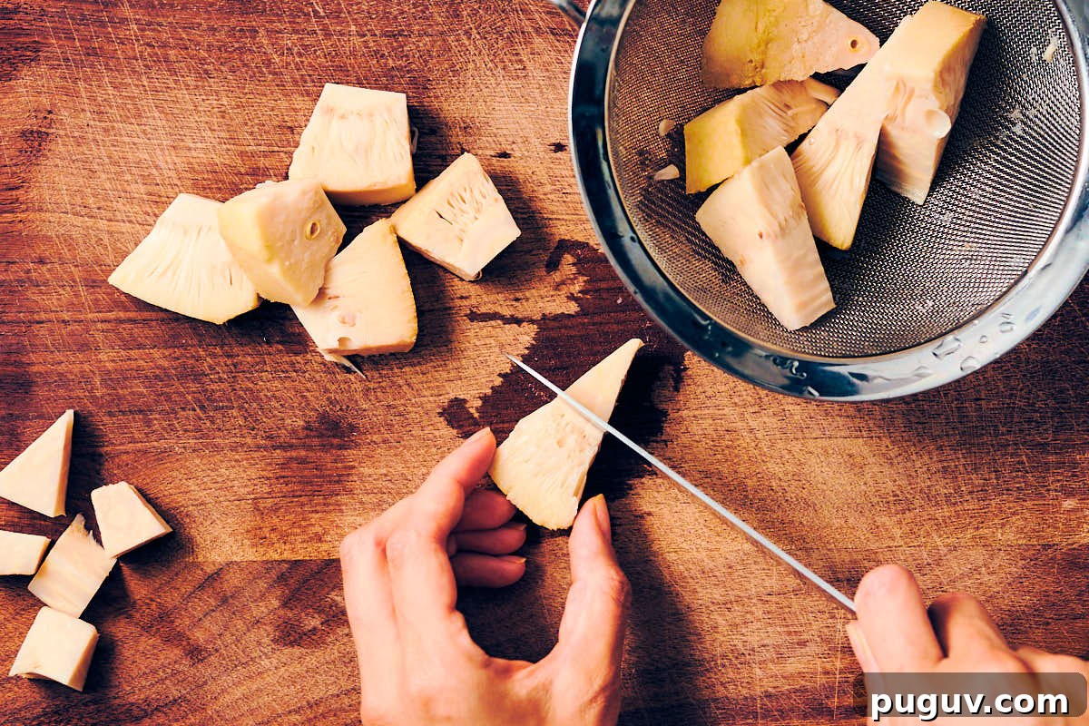 A knife cutting jackfruit on a wood cutting board.