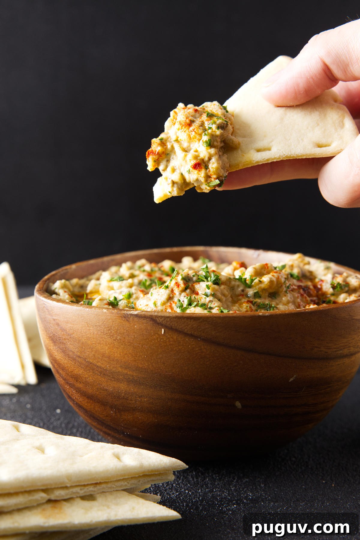 Smoked Baba Ganoush Recipe: Creamy Charred Eggplant Dip 4 Dipping slice of pita bread in to a wooden bowl filled with baba ganoush.
