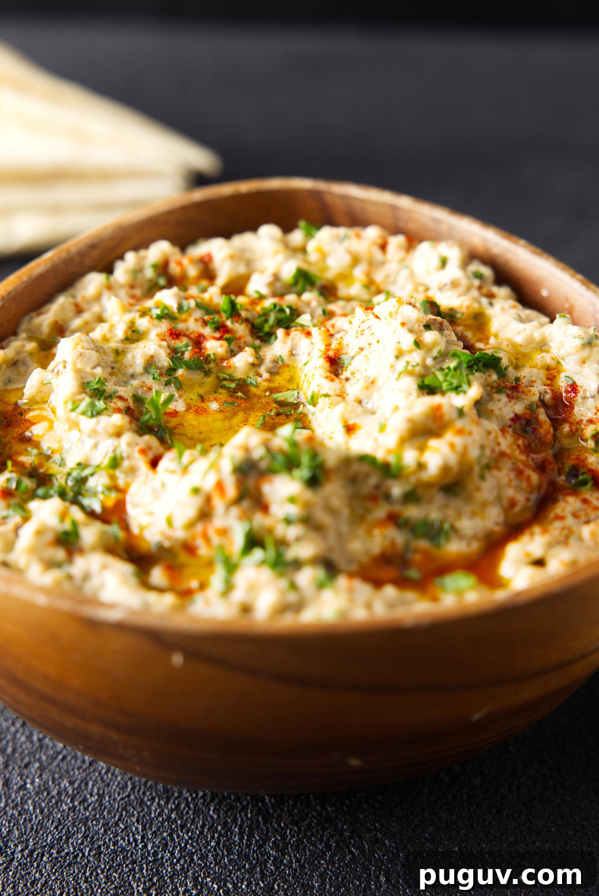 Smoked Baba Ganoush Recipe: Creamy Charred Eggplant Dip 5 Wooden bowl filled to the brim with baba ganoush and topped with a drizzle of olive oil and chopped parsley.