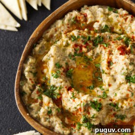 Smoked Baba Ganoush Recipe: Creamy Charred Eggplant Dip 7 Close up of smoked baba ganoush in wooden bowl topped with paprika, chopped parsley, and an olive oil drizzle.