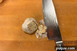 Smoked Baba Ganoush Recipe: Creamy Charred Eggplant Dip 9 Cutting the top off of a bulb of garlic on a wooden cutting board.