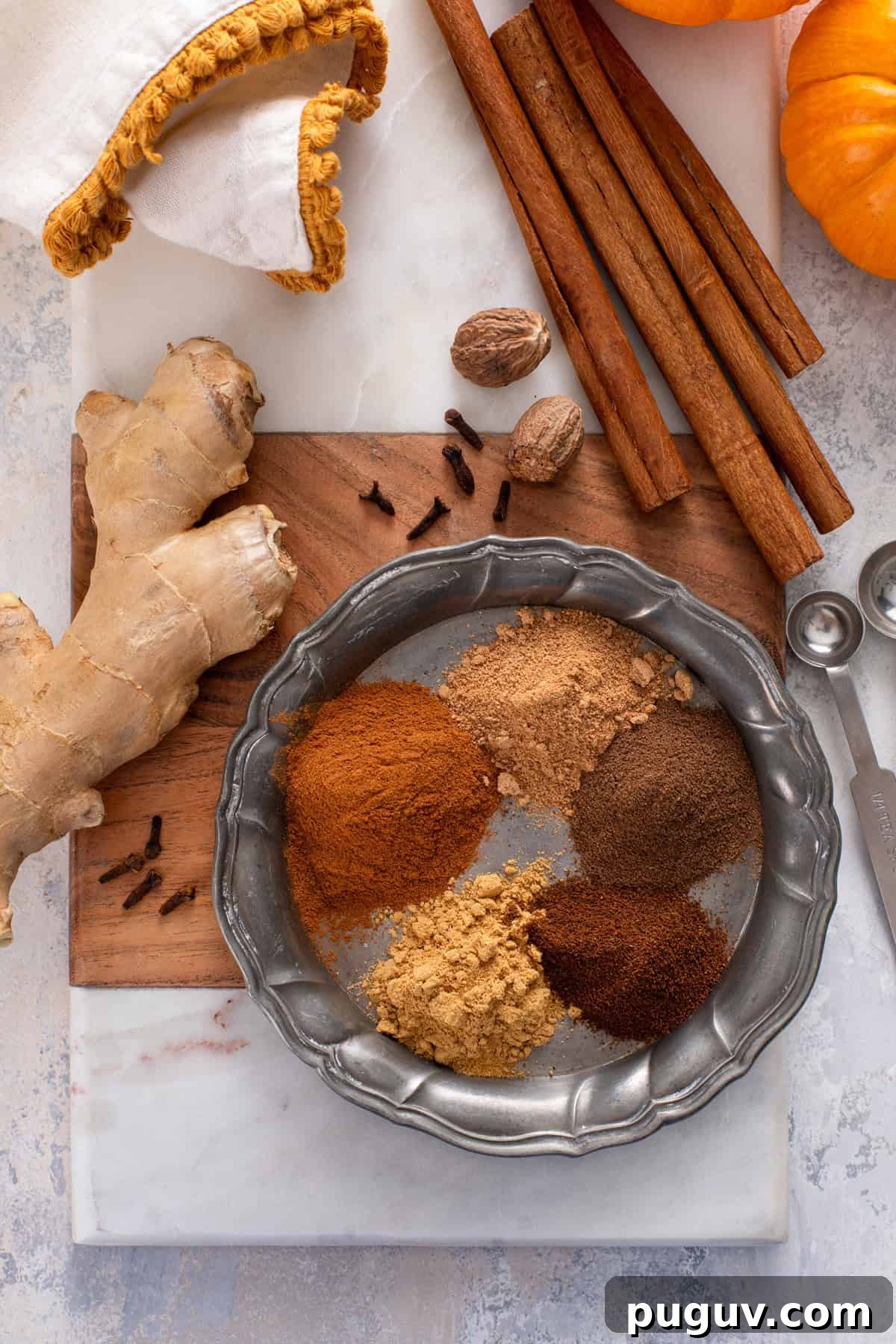 How to Make Pumpkin Pie Spice at Home for Cozy Fall Baking 3 Individual spices for pumpkin pie spice measured out and arranged on a metal plate.