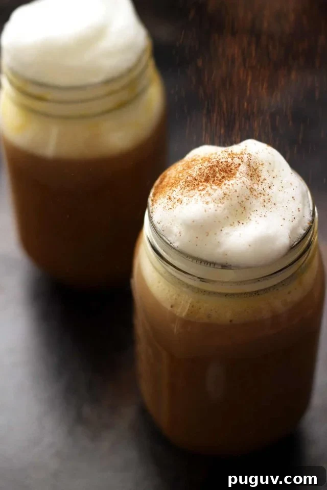 Healthy Vegan Pumpkin Spice Latte in a Mason Jar Topped with Cashew Whipped Milk Being Sprinkled with Cinnamon