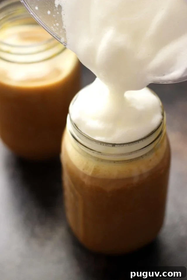 Healthy Vegan Pumpkin Spice Latte in a Mason Jar Topped with Cashew Whipped Milk Being Poured on Top