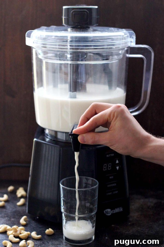 Healthy Vegan Pumpkin Spice Latte - the NutraMilk Dispensing Nut Milk in a Glass with Cashews Lying Around