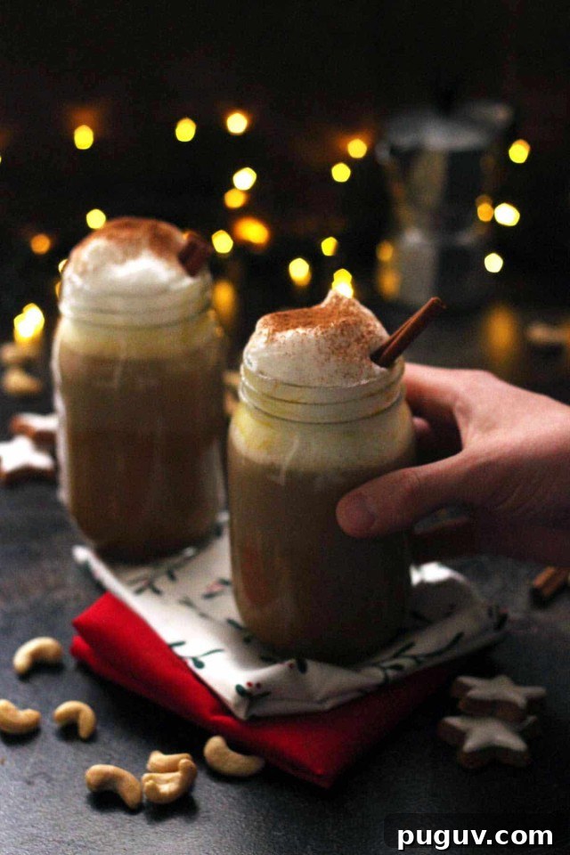 Hand Holding a Glass of Healthy Vegan Pumpkin Spice Latte with Lights and Another Jar in the Background