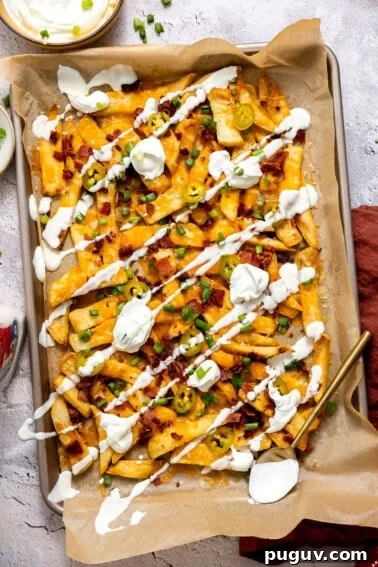 Loaded Texas Nachos Recipe: How to Make Classic Tex-Mex Nachos 18 Golden, crispy French fries loaded with melted cheese, bacon, green onions, and a drizzle of sour cream on a baking tray.
