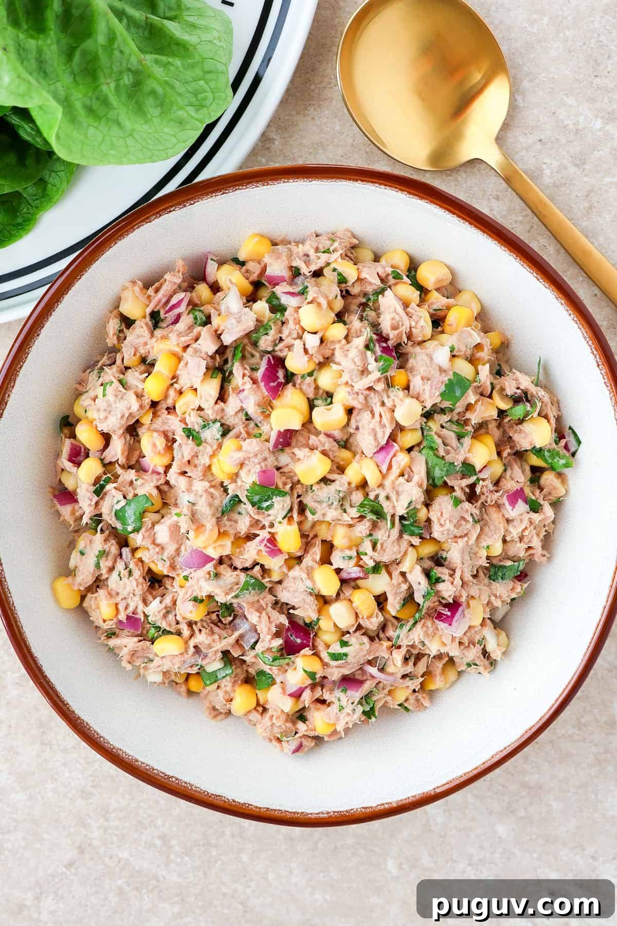 Tuna salad with corn in a bowl with a gold spoon.