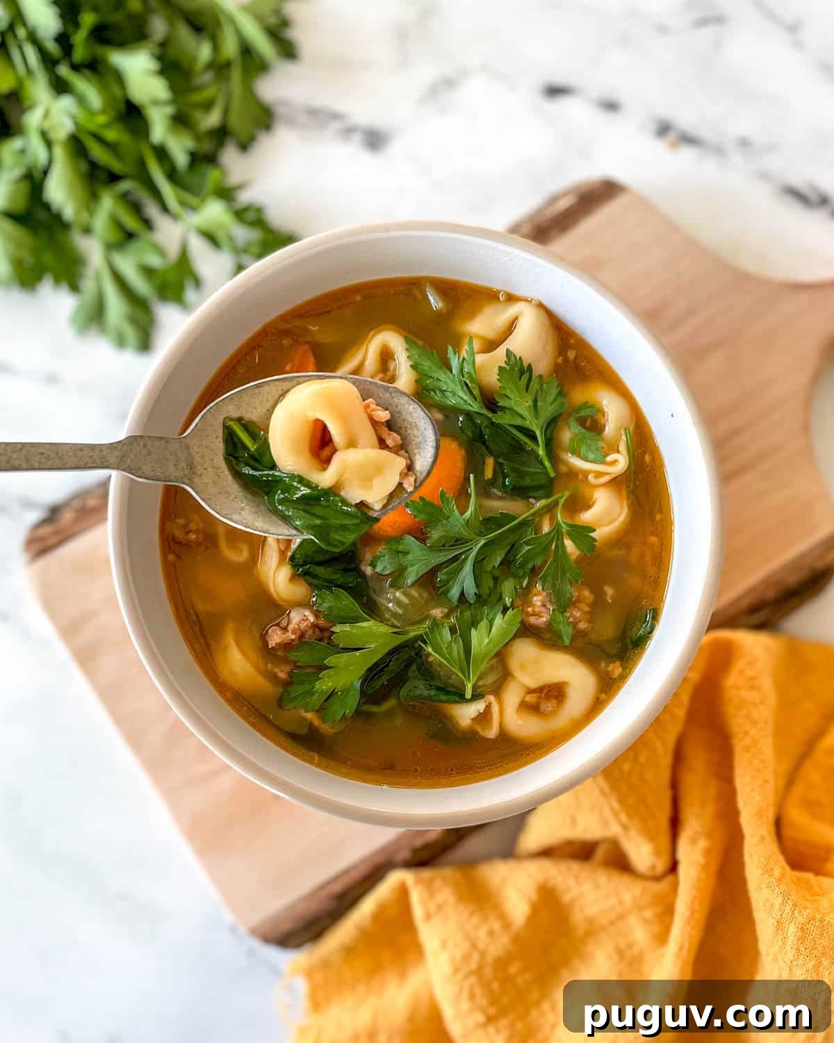 Creamy Instant Pot Tortellini Soup Recipe for Quick Weeknights 2 A bowl of tortellini soup sits on a rustic wooden cutting board with a yellow linen and a bunch of parsley.