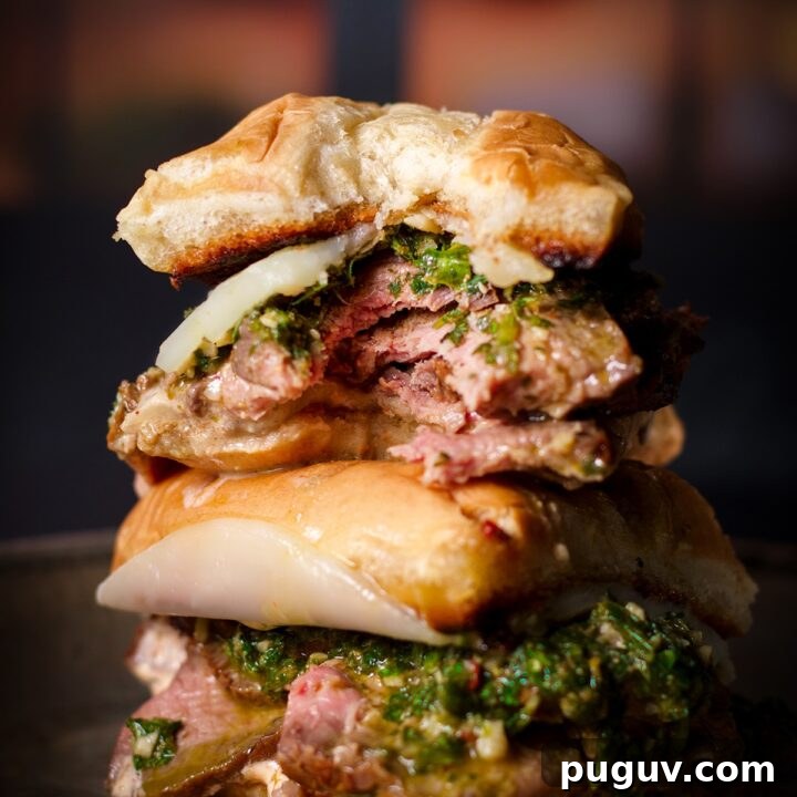 Two halves of a chimichurri steak sandwich, one half stacked on top of the other, with a bite taken out of the top half.
