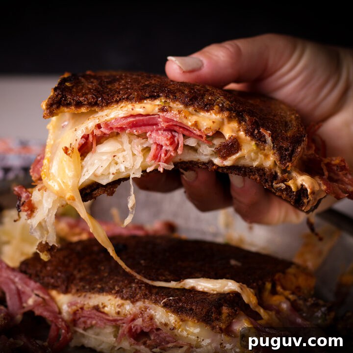 Someone picking up half of a Reuben Sandwich with melted cheese spilling out of it.