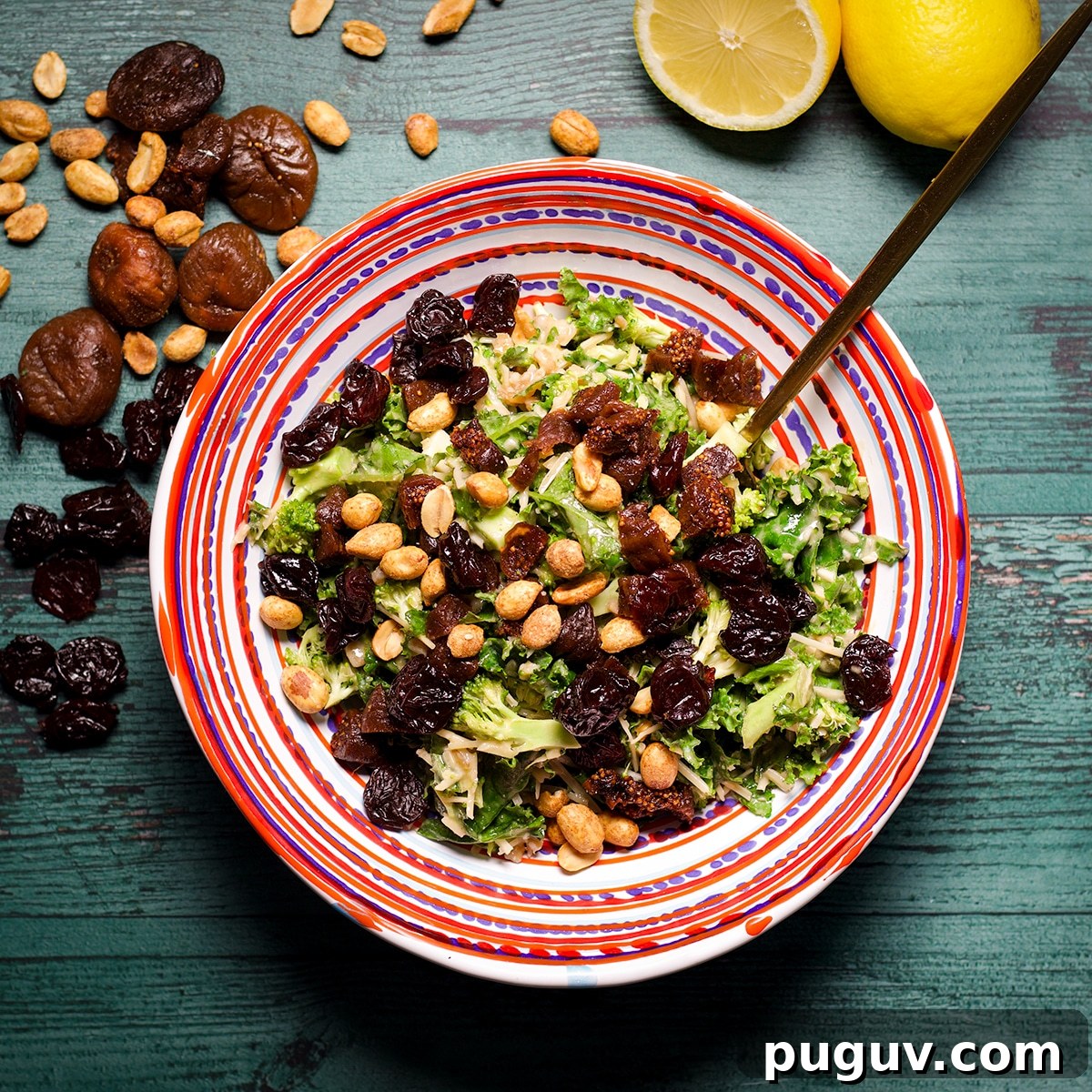 A bowl filled with kale and broccoli salad topped with dried fruit and roasted peanuts.