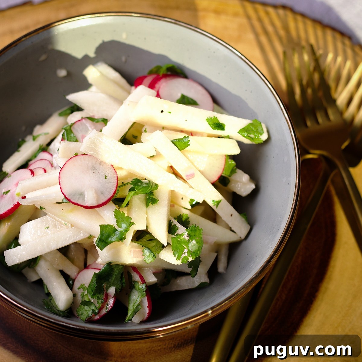 A bowl on a wood serving platter filled with jicama salad with apples.