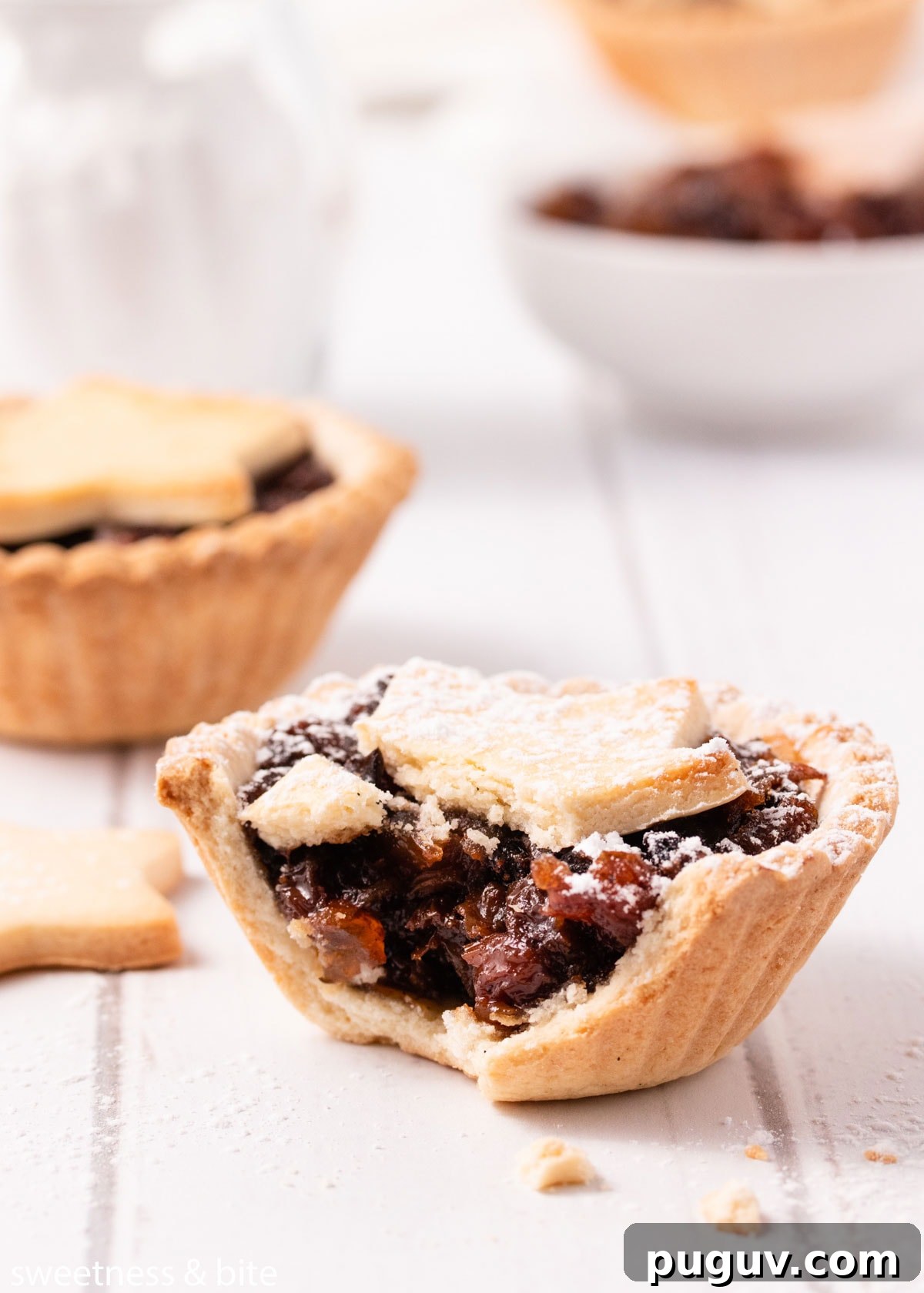 A close up of a bitten mince pie dusted with icing sugar
