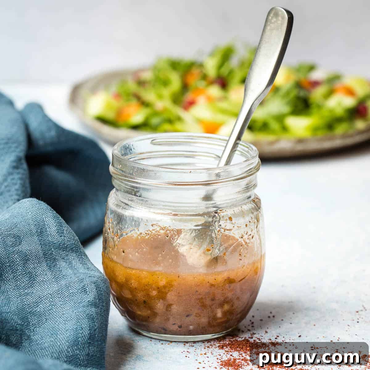 jar of sumac dressing next to blue linen and in front of plate of salad