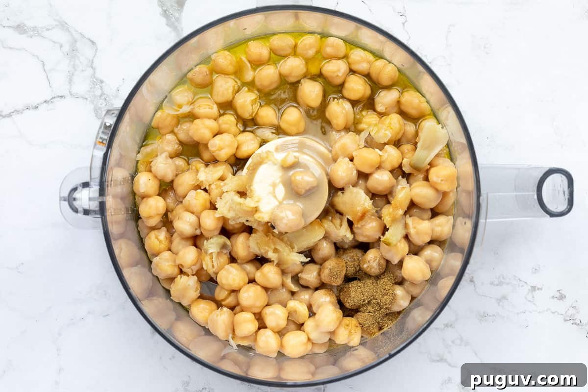 Creamy Roasted Garlic Hummus Recipe for Smooth, Flavorful Dip 4 roasted garlic hummus ingredients in bowl of food processor before blending.