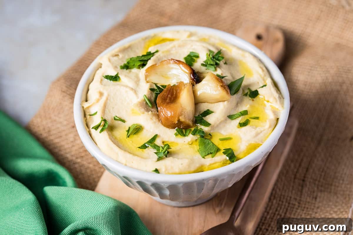 Creamy Roasted Garlic Hummus Recipe for Smooth, Flavorful Dip 8 bowl of roasted garlic hummus on cutting board over burlap next to green napkin.