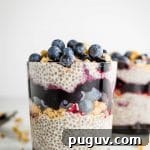 Berry Chia Pudding with Crunchy Granola Bowl PMID 5 A glass filled with layered chia seed pudding with granola, jam and fresh blueberries.