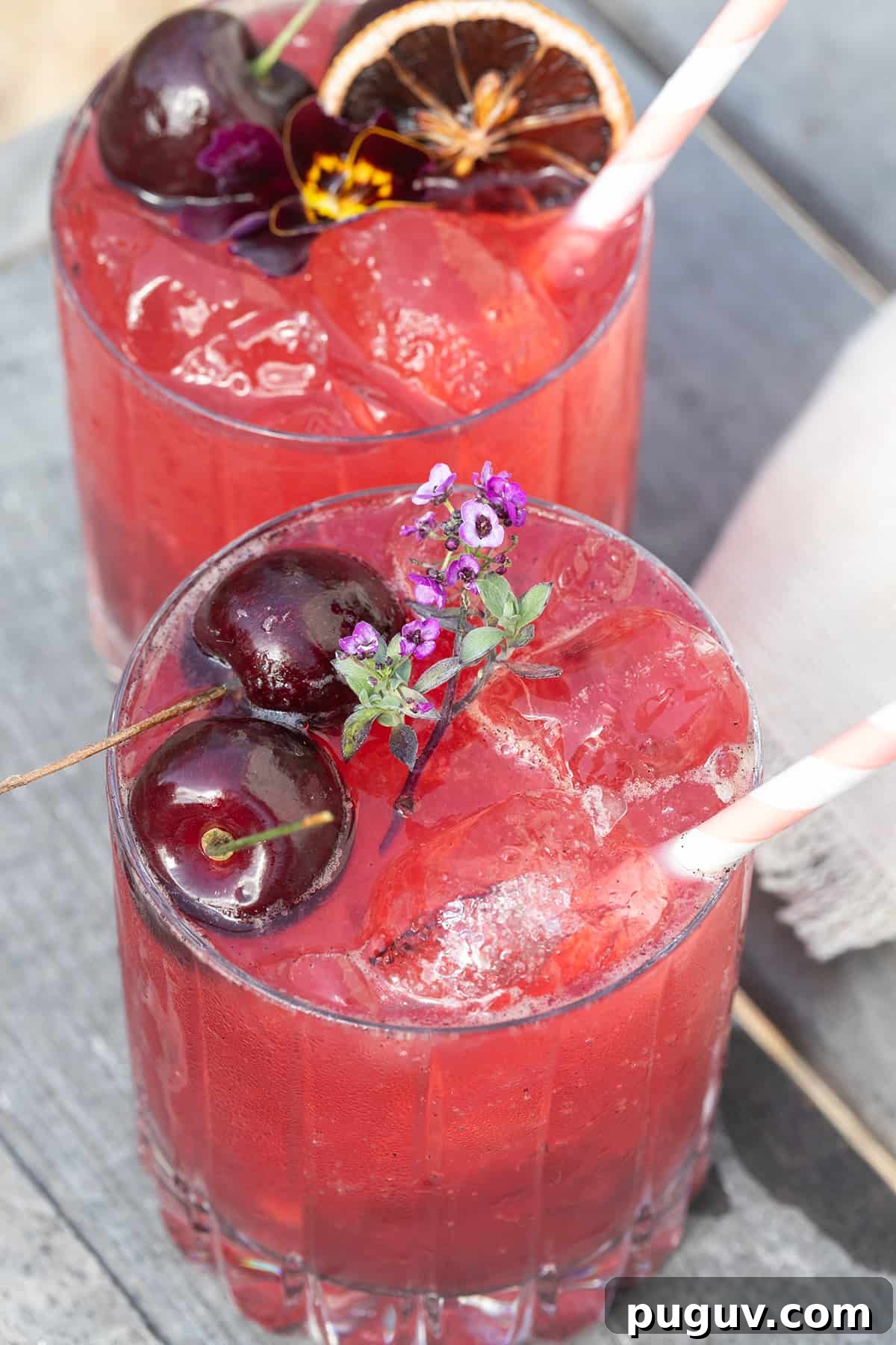 A cherry gin soda with cherries, edible flowers and a stripy straw.