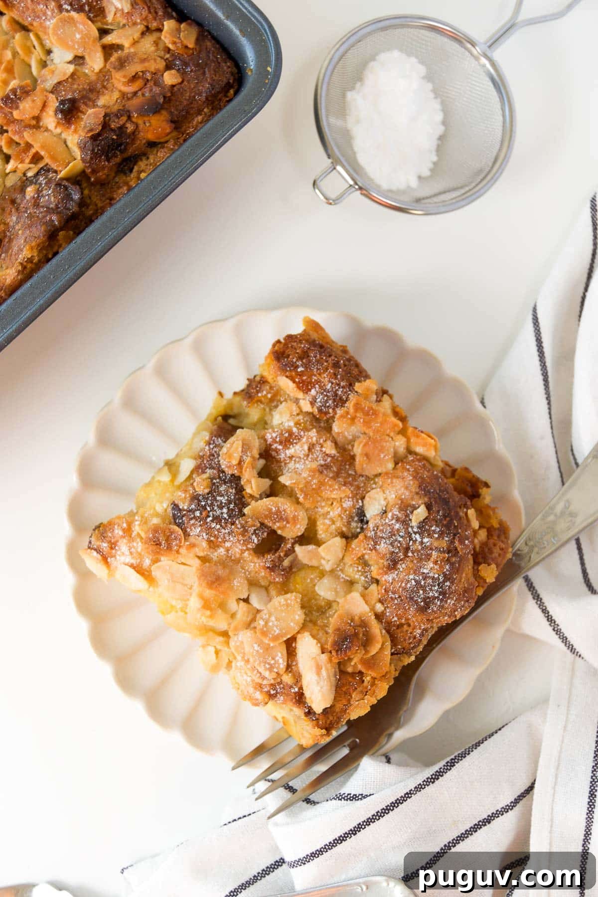 Panettone Bread Pudding Recipe: Decadent Holiday Dessert 2 a slice of panettone bread pudding on a white scalloped plate with a fork next to a square pan of more bread pudding
