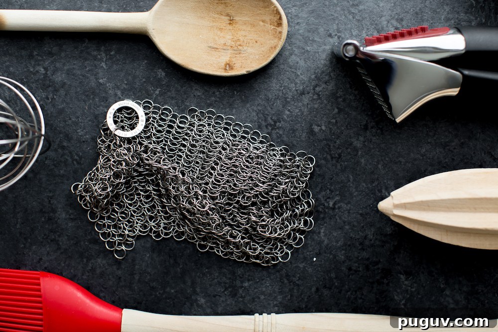 kitchen equipment including garlic press citrus reamer wooden spoon and chain link scrubber on dark background