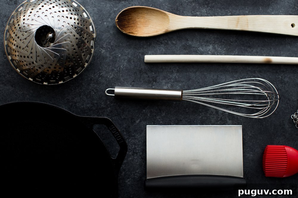 kitchen equipment including whisk steamer wooden spoon bench scraper and cast iron skillet on dark background