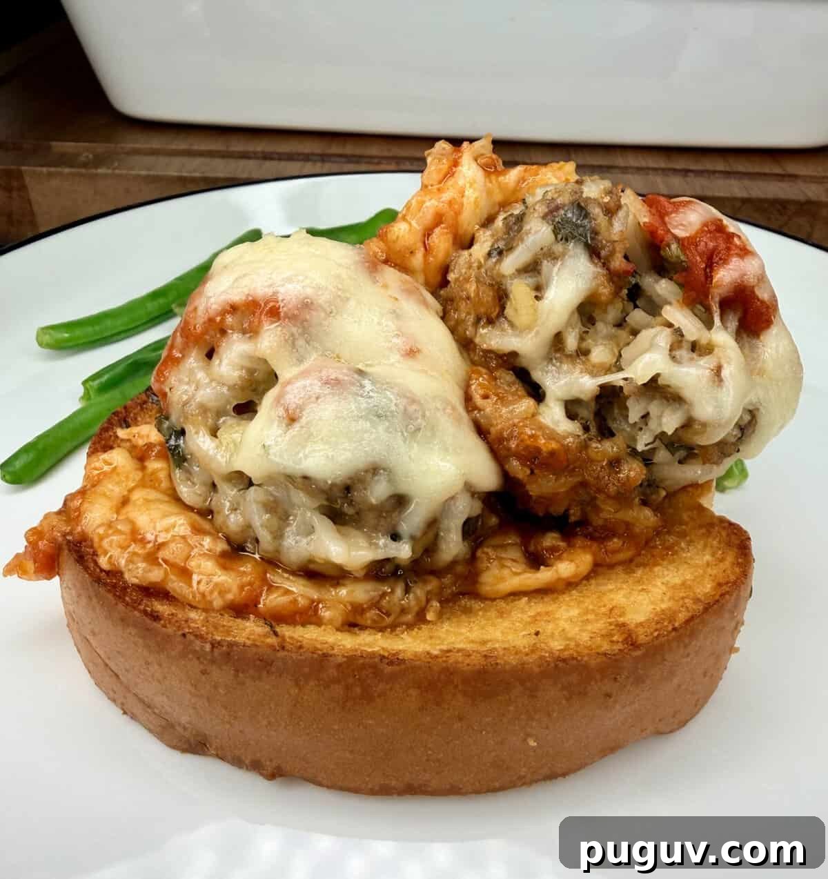 Italian-Style Baked Rice and Meatball Casserole 14 Two cheesy baked meatballs topped with marinara sauce sit on a thick slice of toasted bread, with green beans in the background on a white plate.