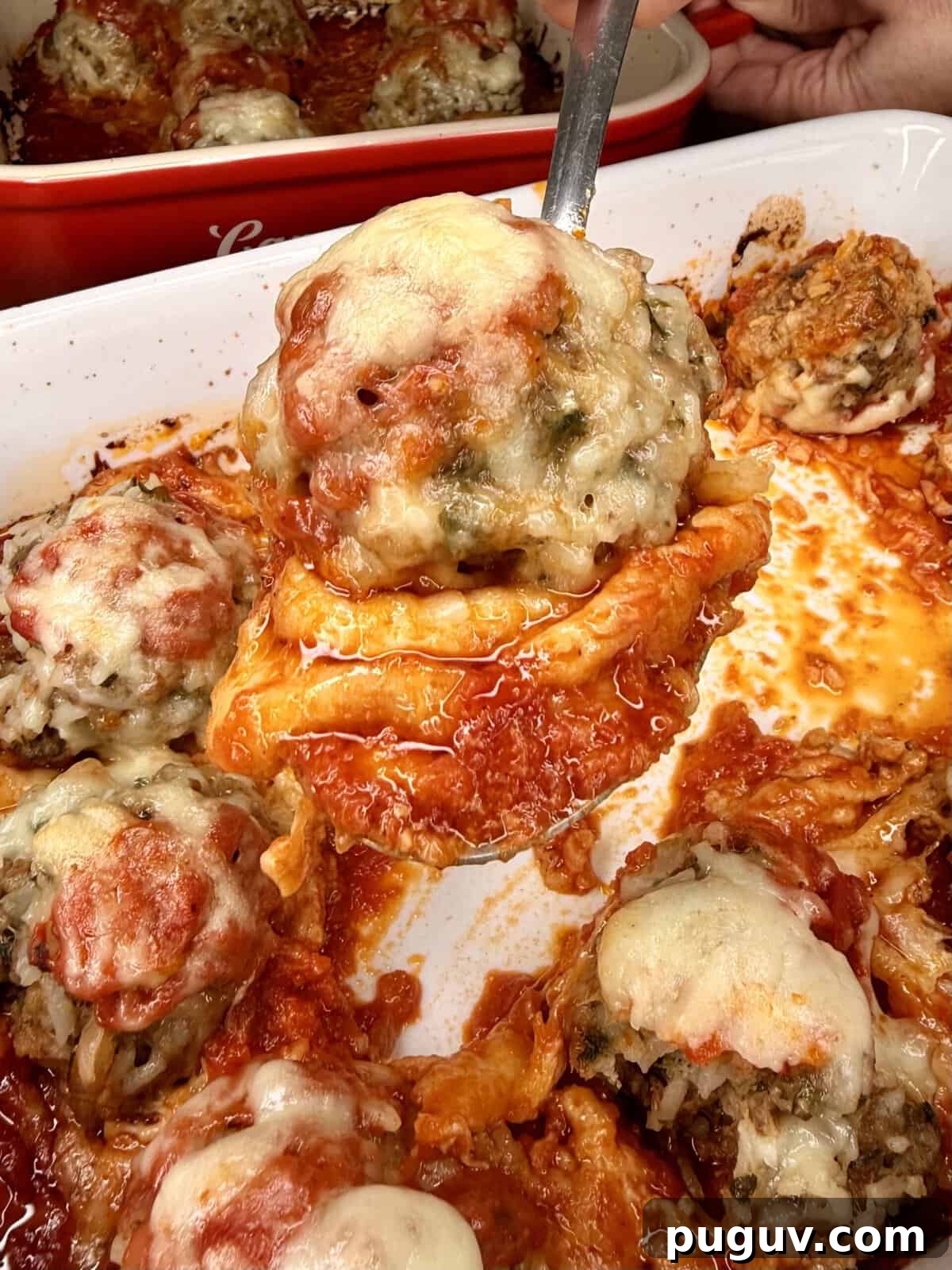Italian-Style Baked Rice and Meatball Casserole 16 A close-up of a cheesy stuffed pepper being lifted from a baking dish, surrounded by several other stuffed peppers topped with melted cheese and tomato sauce.