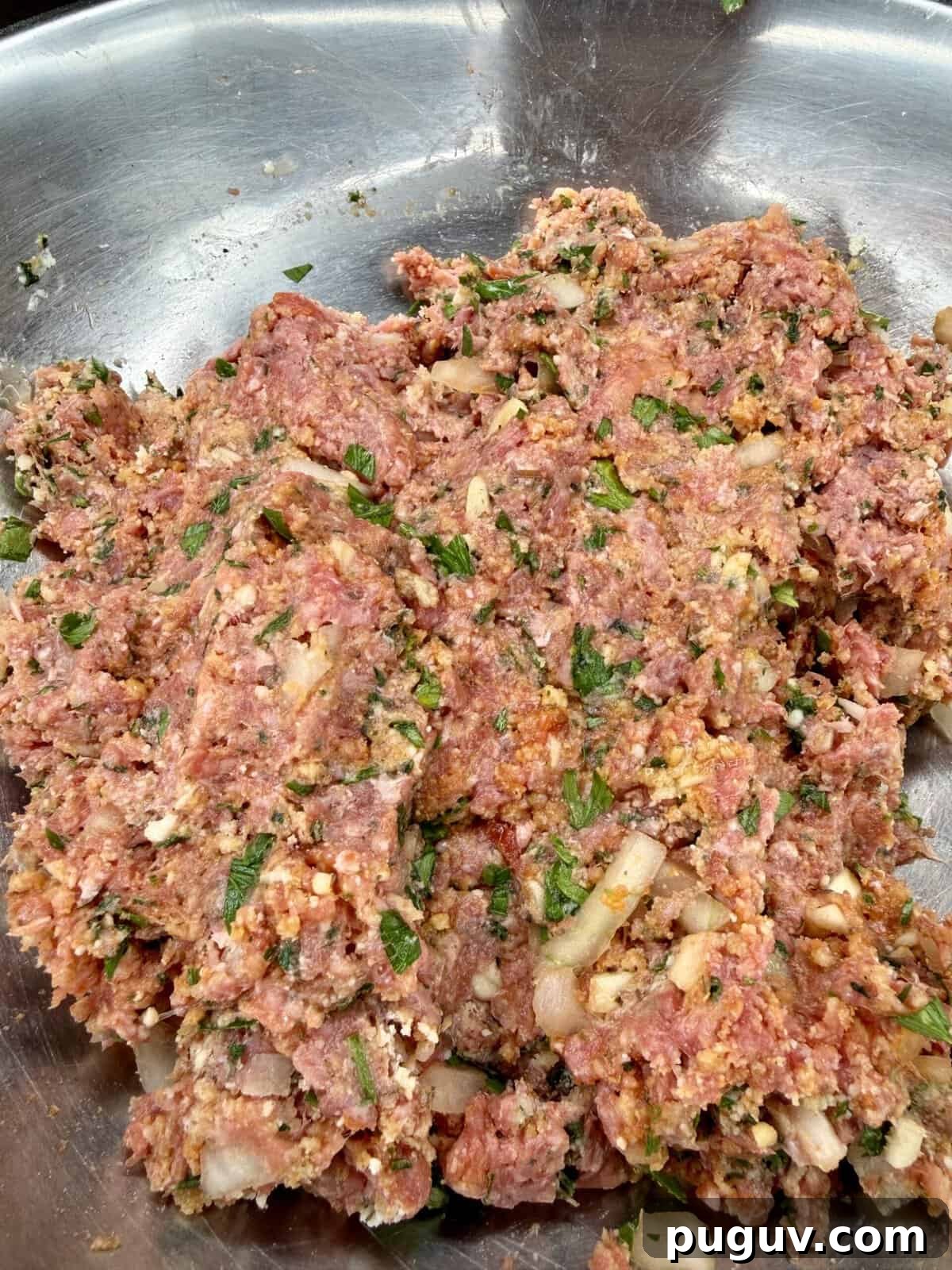 Italian-Style Baked Rice and Meatball Casserole 4 A close-up of a metal bowl filled with raw ground meat mixed with chopped onions, herbs, and spices, ready to be cooked or formed into patties.