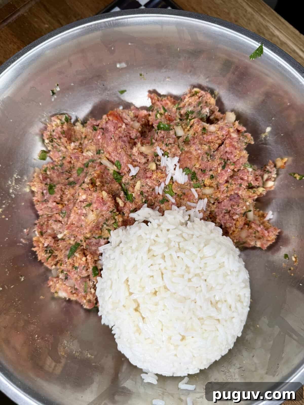 Italian-Style Baked Rice and Meatball Casserole 5 A metal bowl containing a mixture of ground meat, herbs, and spices, with a mound of cooked white rice placed on top of the mixture.