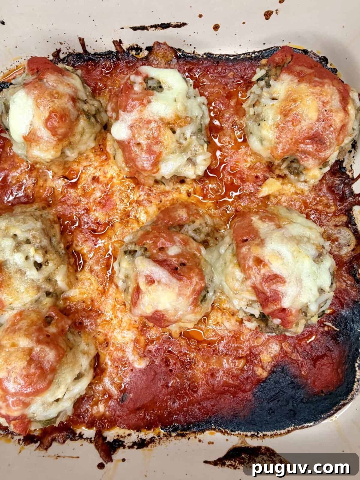 Italian-Style Baked Rice and Meatball Casserole 10 Seven baked meatballs topped with melted cheese and marinara sauce sit in a baking dish. The edges of the sauce are browned and caramelized, giving a slightly crispy appearance around the dish.