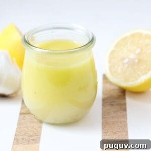 Lemon Garlic Salad Dressing Recipe: Bright Homemade Vinaigrette 5 Lemon garlic salad dressing in a glass jar on a white and wooden board with fresh lemon halves and garlic.