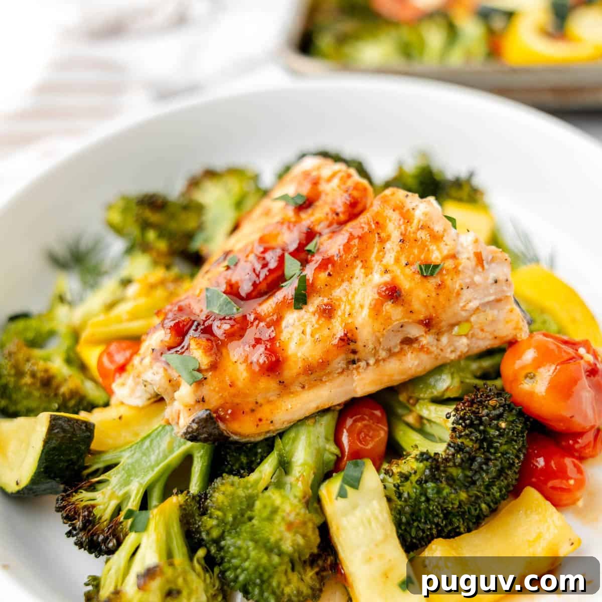 Baked salmon fillet with glaze on roasted broccoli, zucchini, cherry tomatoes on a white plate.