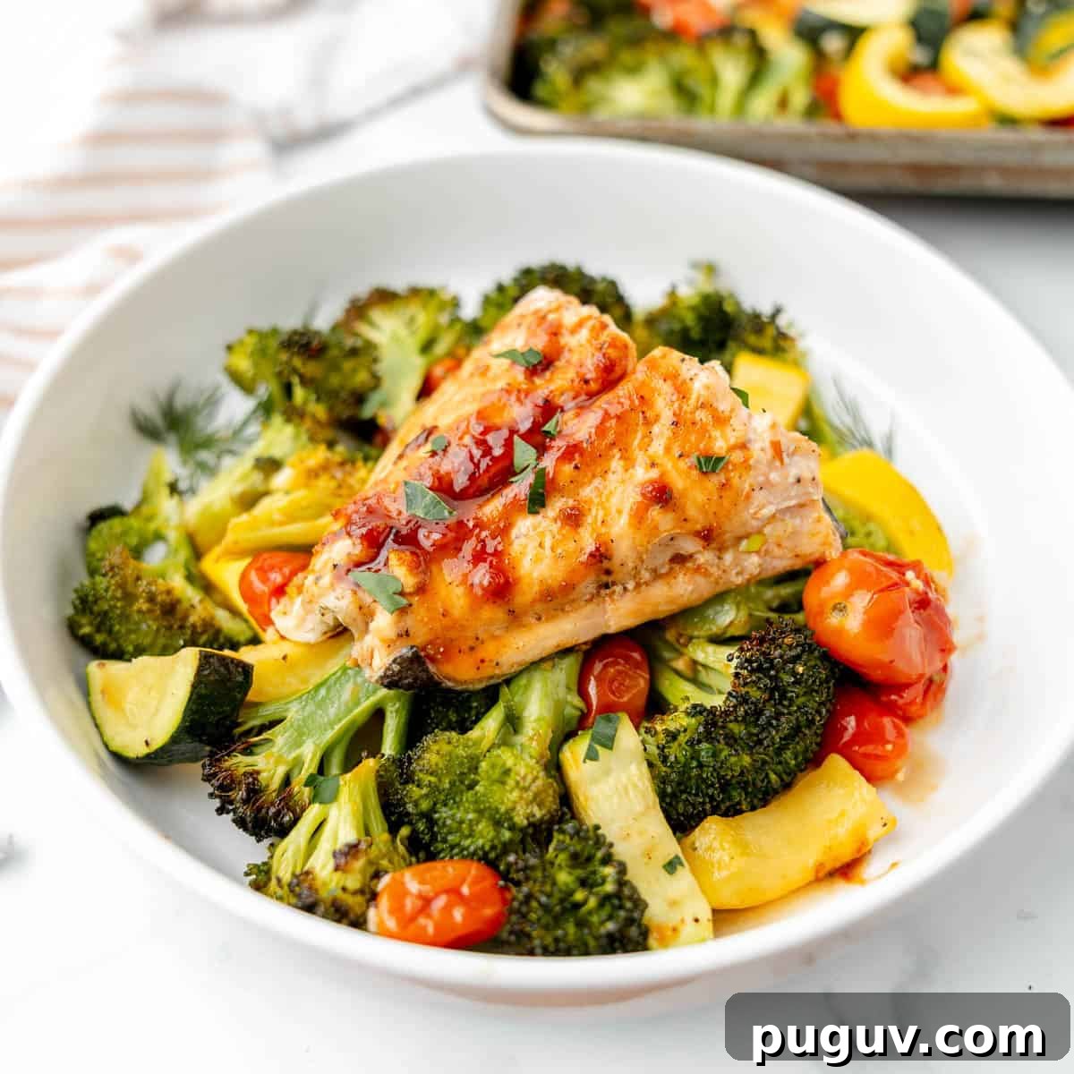 A plate with salmon on a bed of broccoli, zucchini, cherry tomatoes, and yellow squash, garnished with herbs.