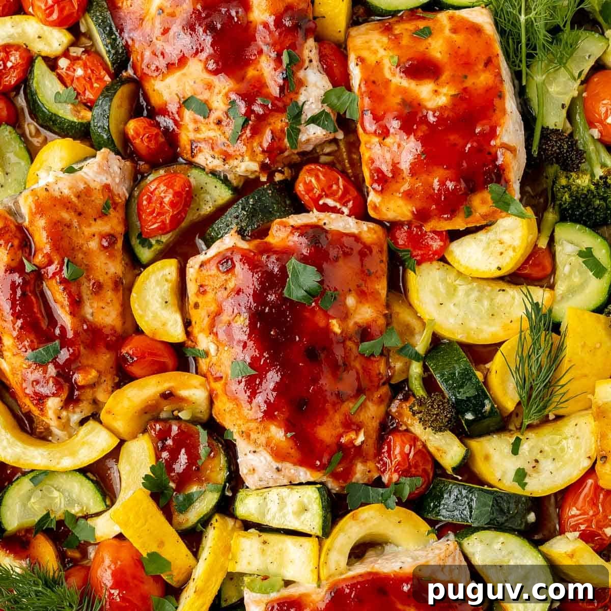 Baked salmon pieces glazed with sauce on a bed of roasted vegetables, including zucchini, squash, tomatoes, and broccoli, garnished with fresh herbs.